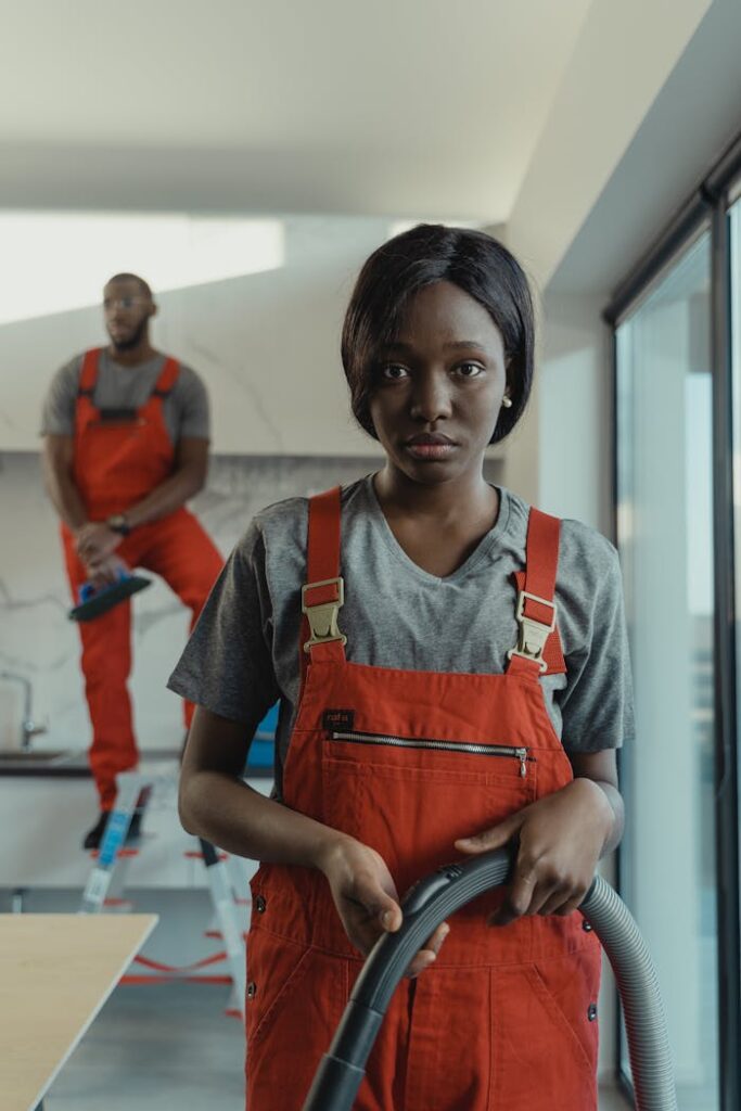 Focused cleaning team in red overalls using vacuum indoors. Modern and efficient service.
